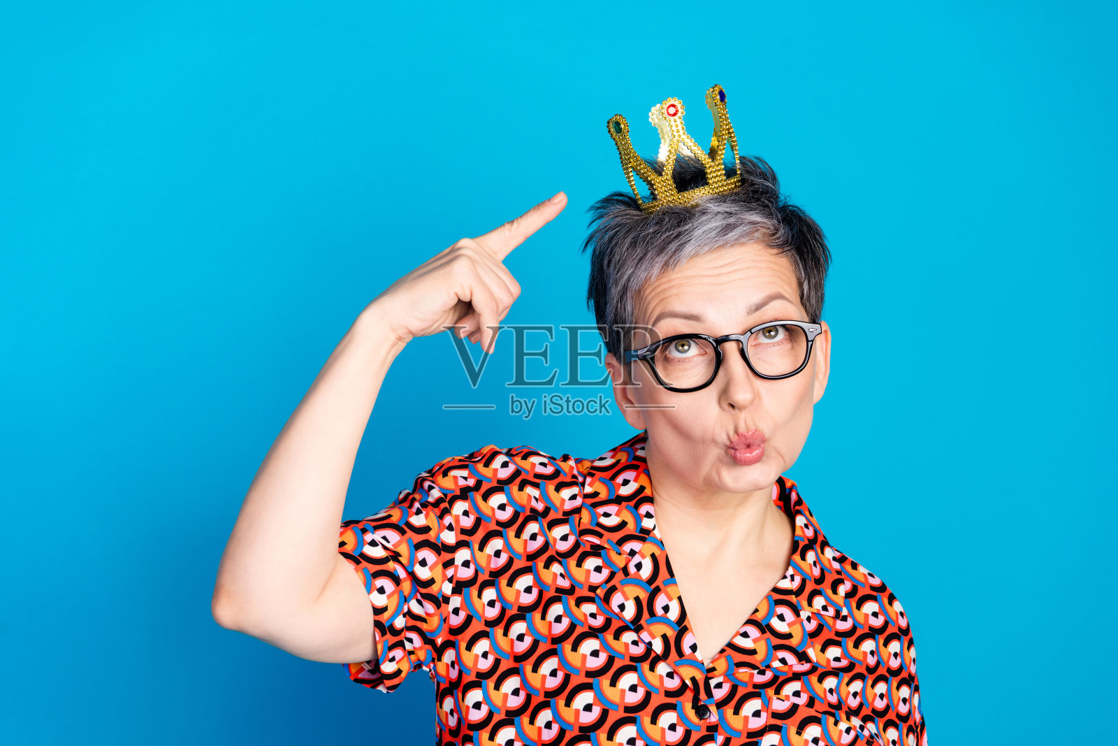 时尚的老年女性在蓝色背景上做出戴冠手势照片摄影图片