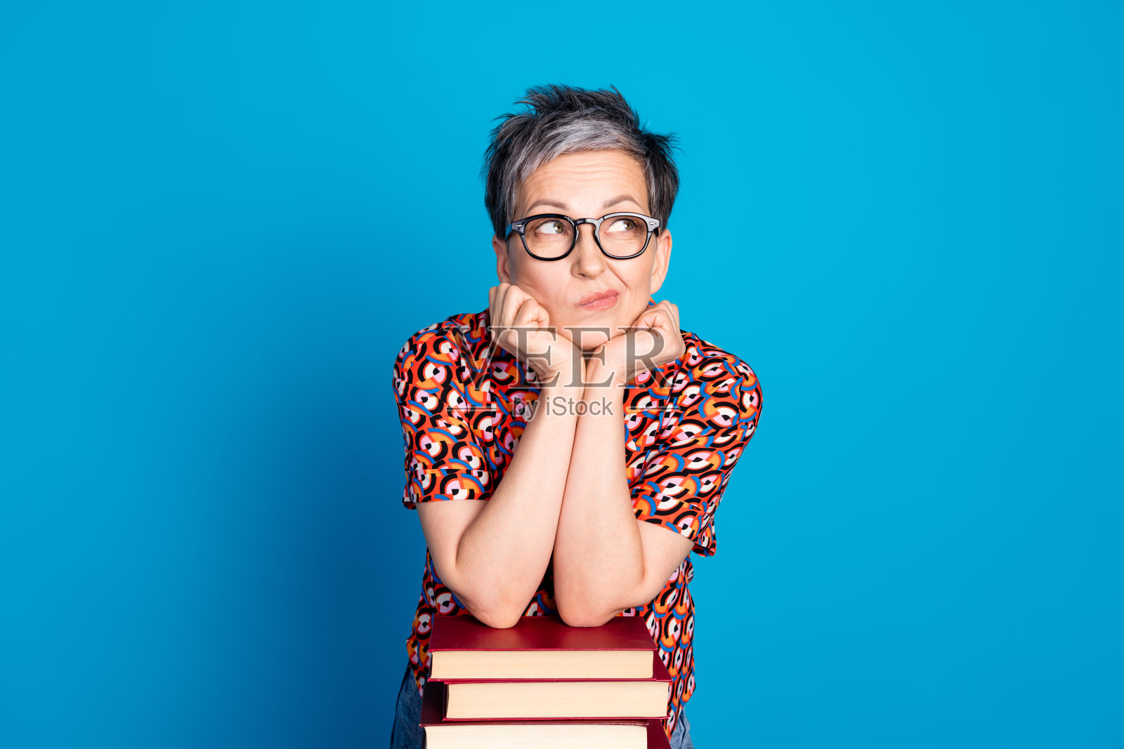 迷人的女性在蓝色背景前深思熟虑地摆姿势，展现时尚与智慧照片摄影图片