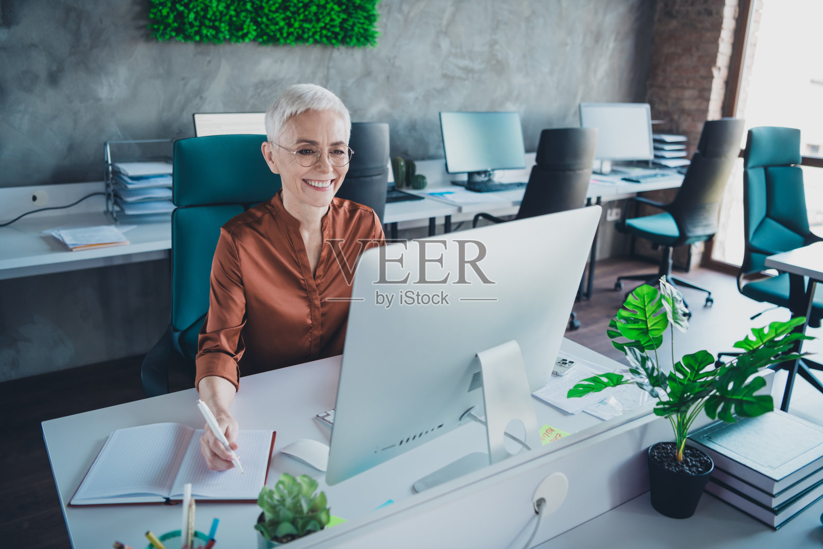 专业成熟的女性企业领导在明亮的办公室中穿着棕色衬衫使用电脑工作照片摄影图片