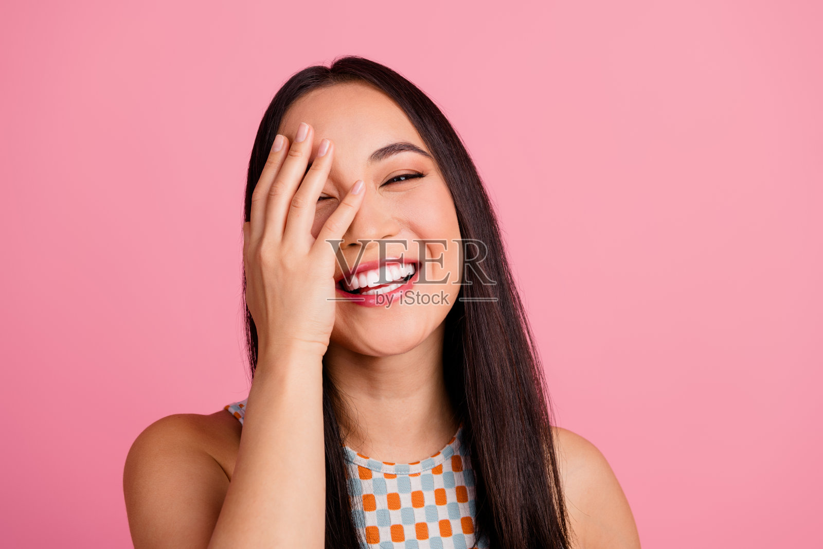 快乐的年轻女性，长棕色头发，在粉色背景下表达幸福感照片摄影图片