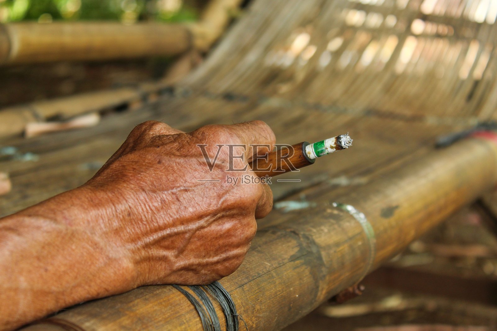 老人的手握着一根用木头制成的烟斗抽烟。照片摄影图片