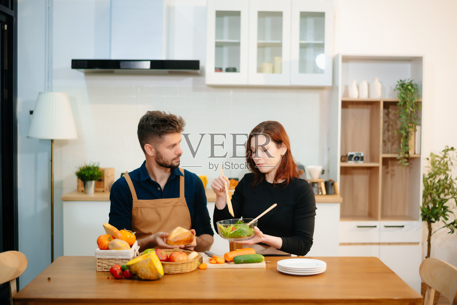快乐的新婚夫妇在温馨的厨房里一起烹饪，准备新鲜的蔬菜和水果。照片摄影图片