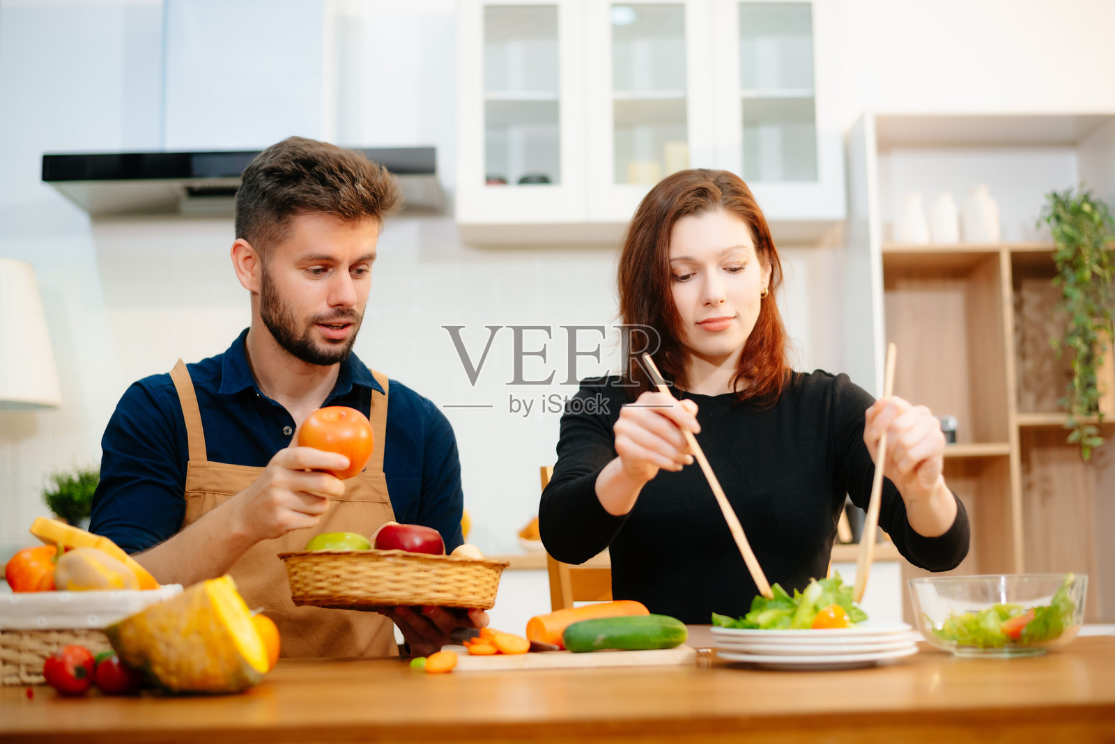 快乐的新婚夫妇在温馨的厨房里一起烹饪，准备新鲜的蔬菜和水果。照片摄影图片