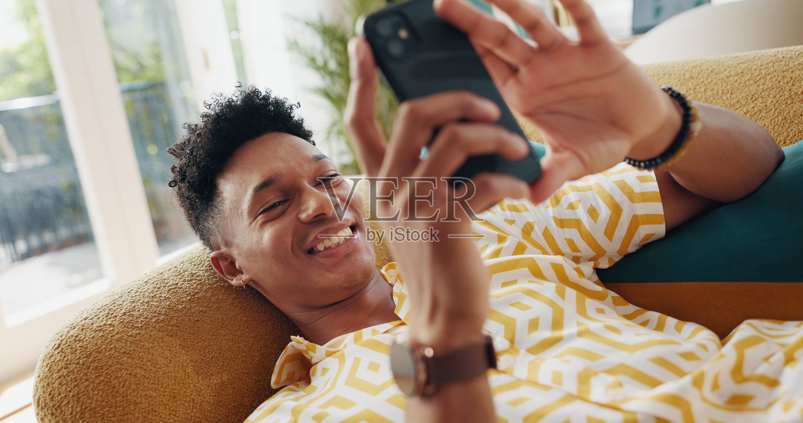 在沙发上放松和快乐的男人，阅读电子书或社交媒体内容创作者的帖子。手机、家和人在聊天应用中进行沟通，查看通知和在线玩游戏。照片摄影图片