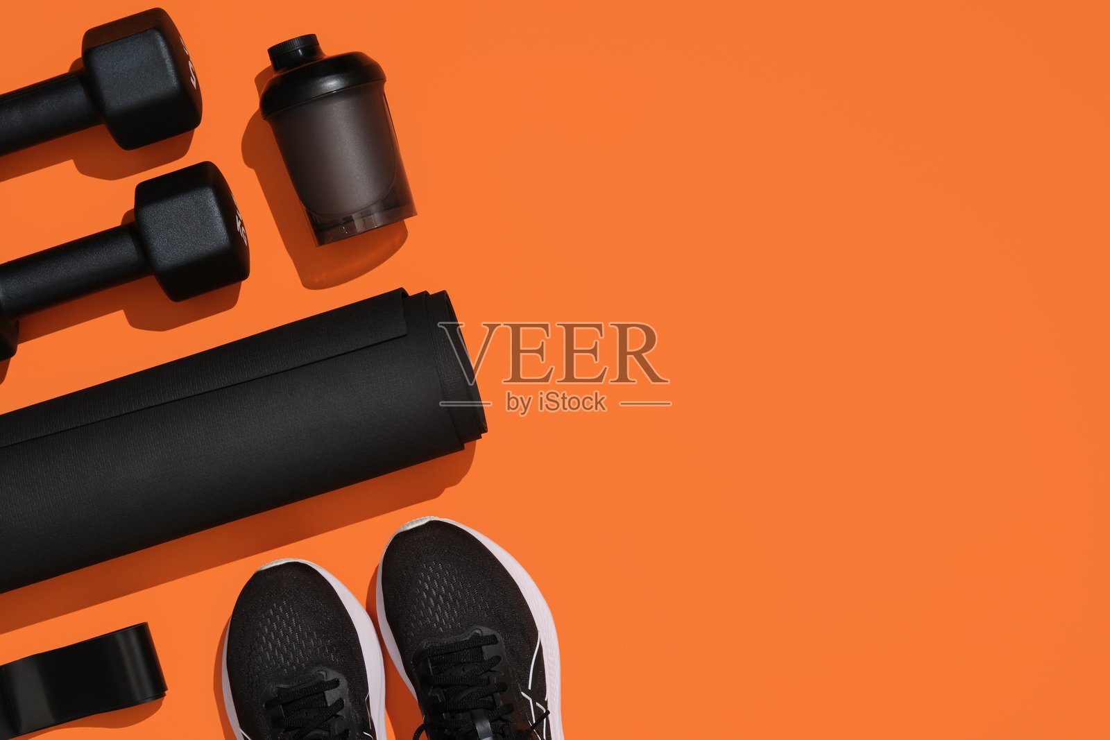 黑色健身器材，哑铃，垫子，弹力带，健身带，水瓶和运动鞋在橙色背景上。健身，运动用品，健康生活方式。您的文本位置。照片摄影图片