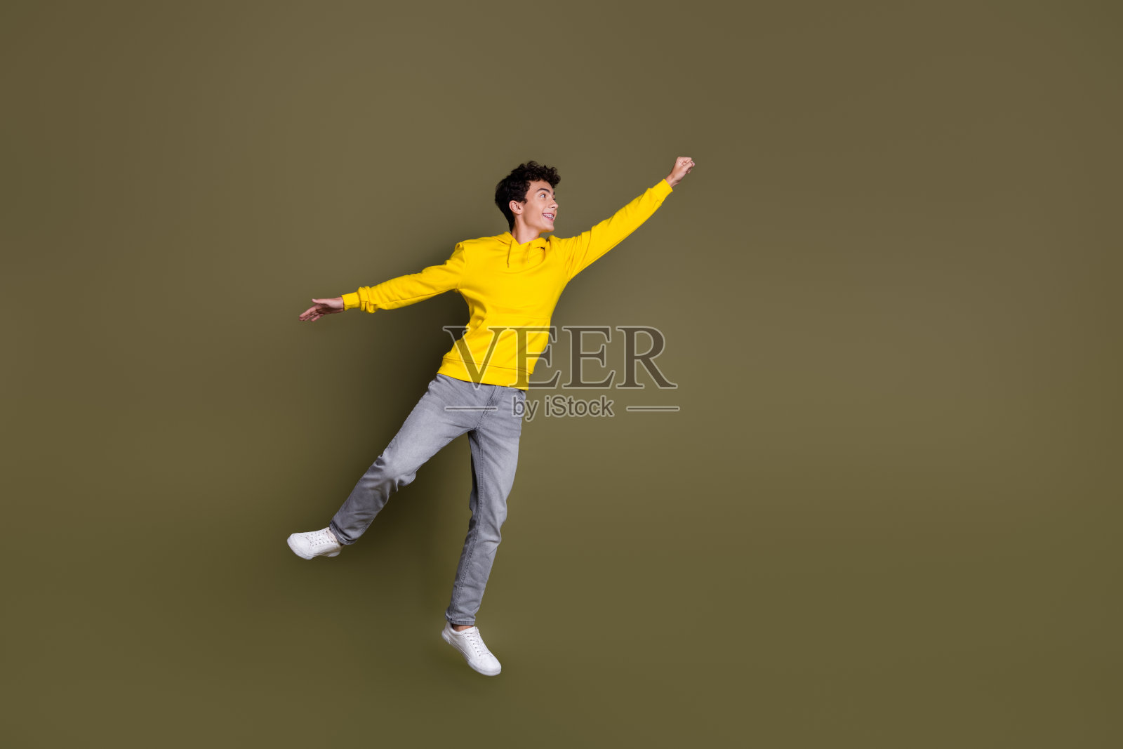 自信的年轻男性穿着休闲服装，站在卡其色背景前，散发出青春活力和俏皮魅力。照片摄影图片