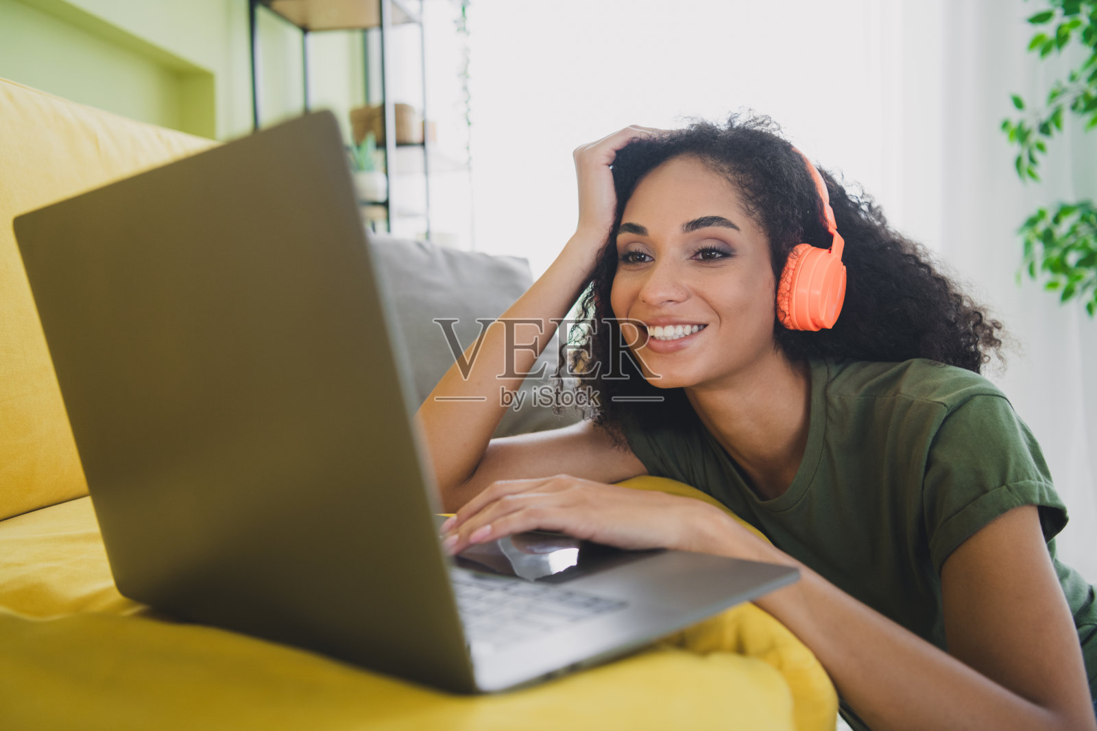 年轻漂亮的女性在室内公寓的客厅里使用笔记本电脑，戴着音乐耳机，阳光明媚。照片摄影图片