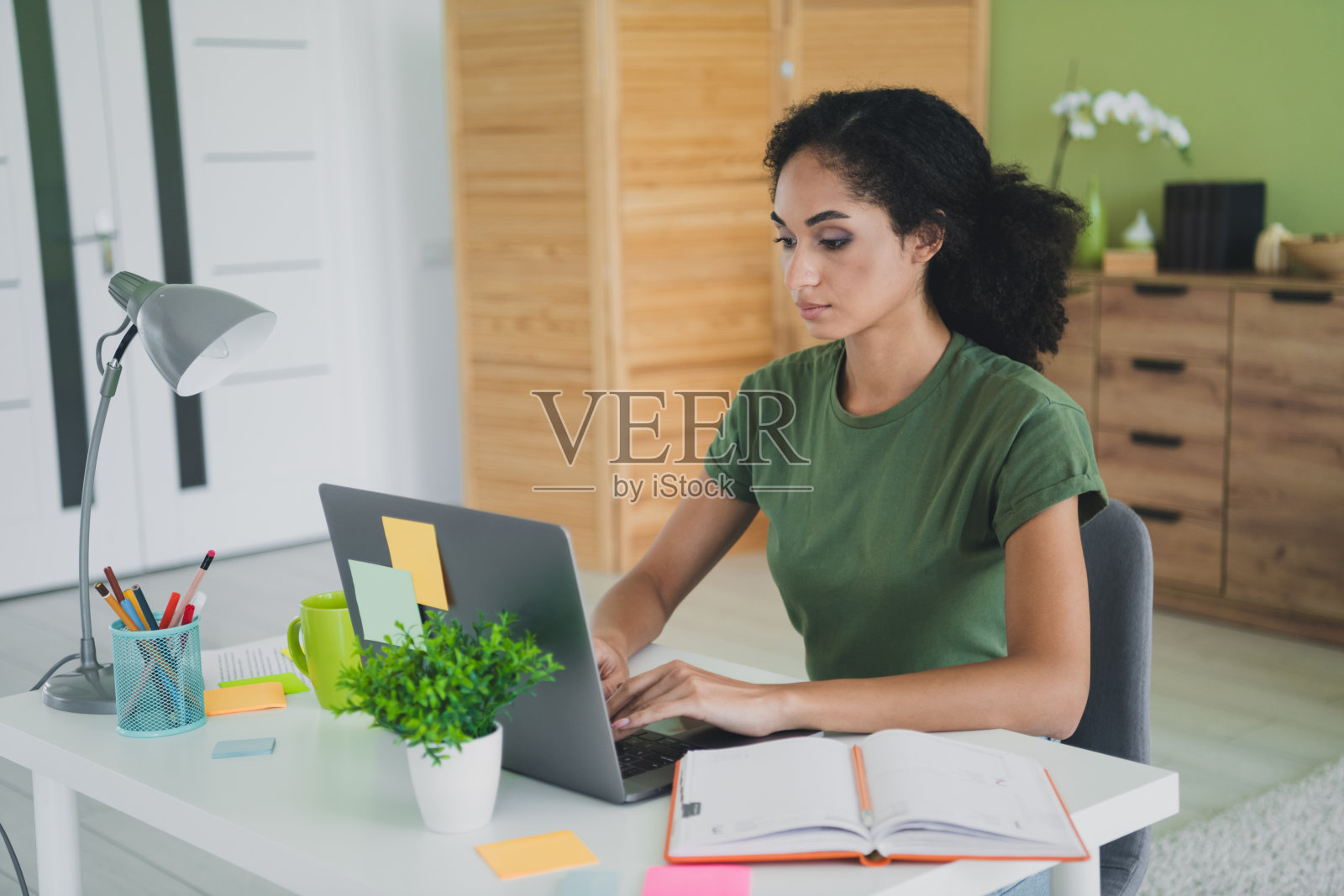 年轻女孩穿着绿色衣服，在现代舒适的家居办公室里使用笔记本电脑工作。照片摄影图片