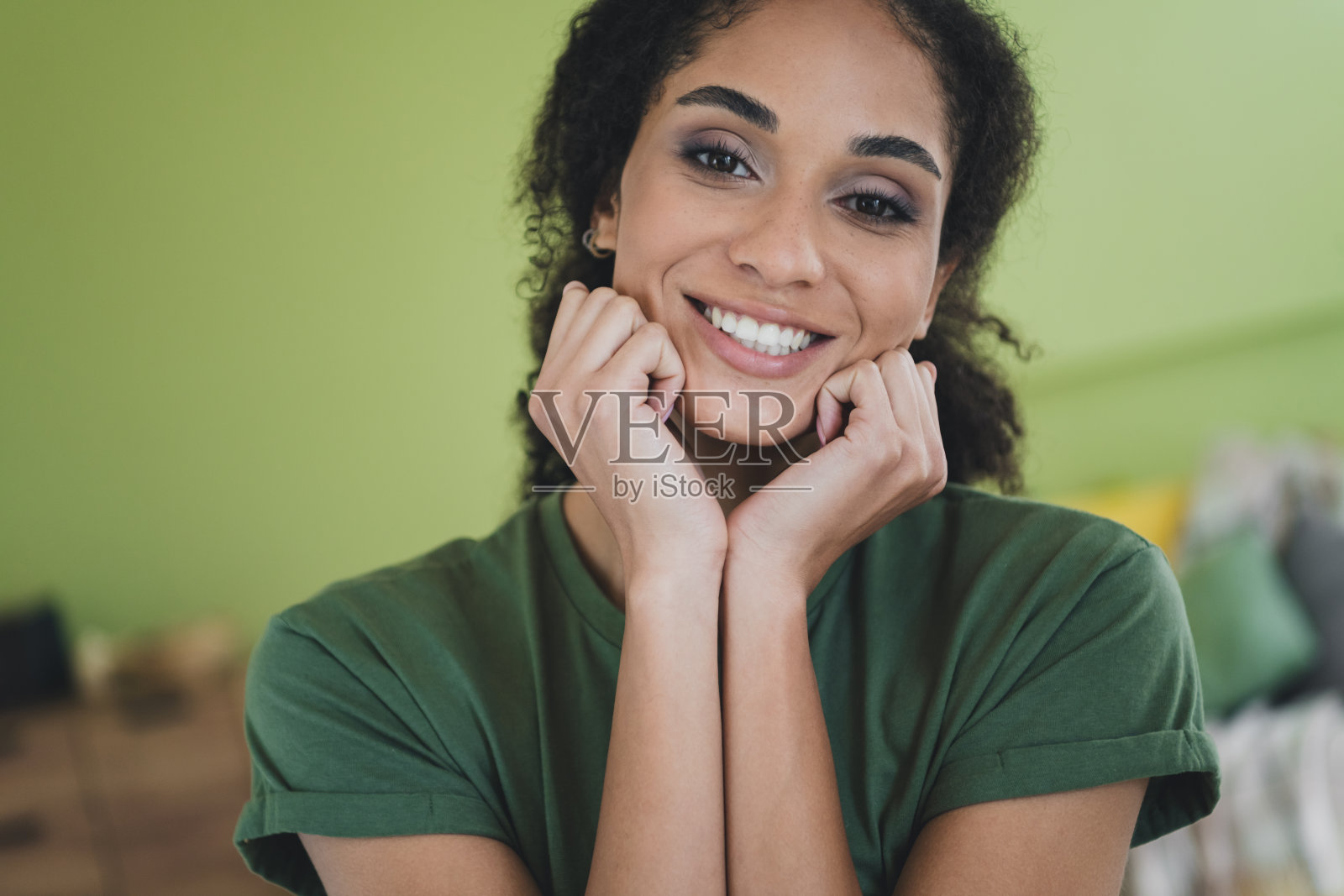 漂亮年轻女孩梦幻般地用拳头触碰脸颊，穿着绿色衣服，享受现代舒适的室内公寓。照片摄影图片