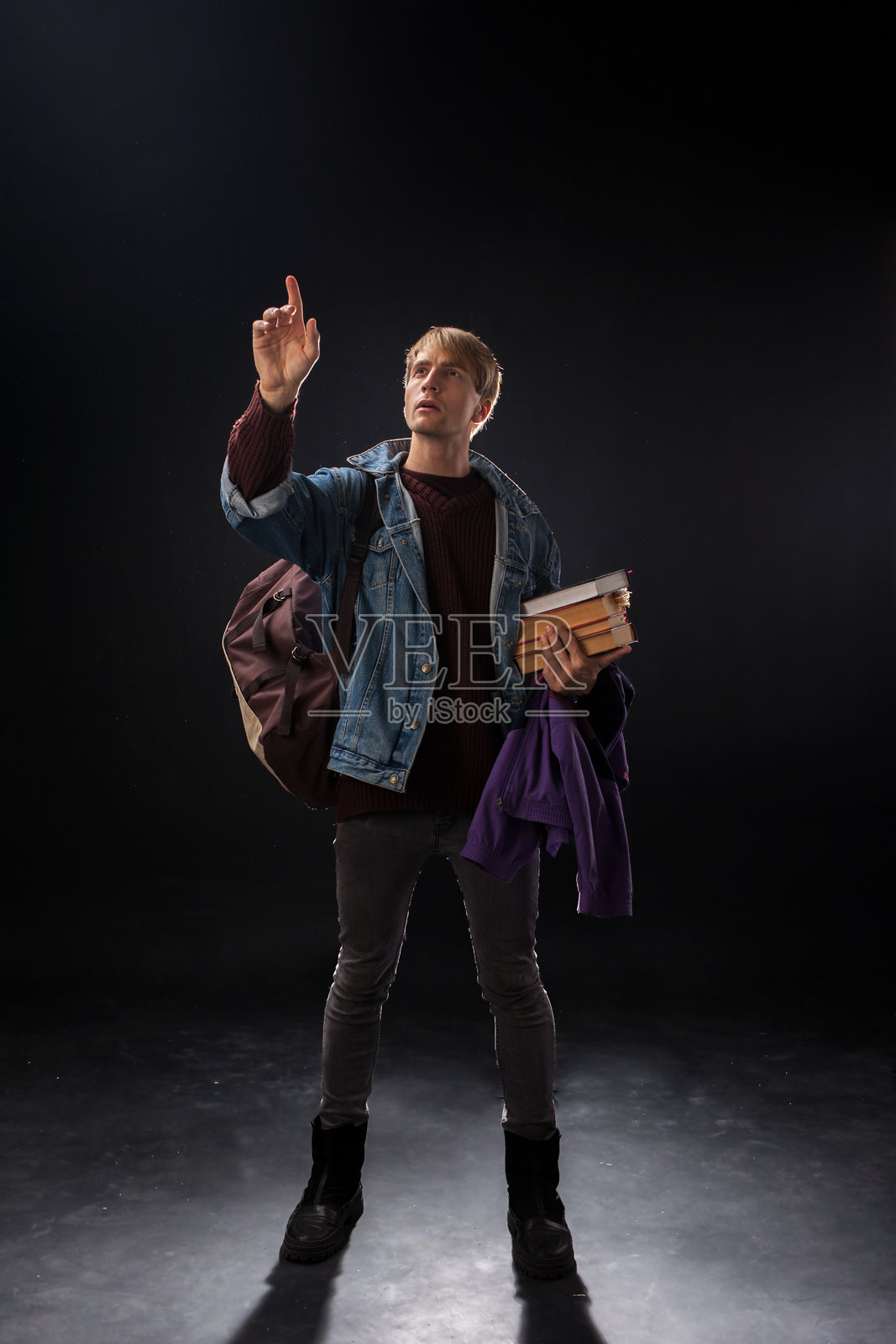 在昏暗的工作室里，一个穿着牛仔夹克和酒红色毛衣的人照片摄影图片