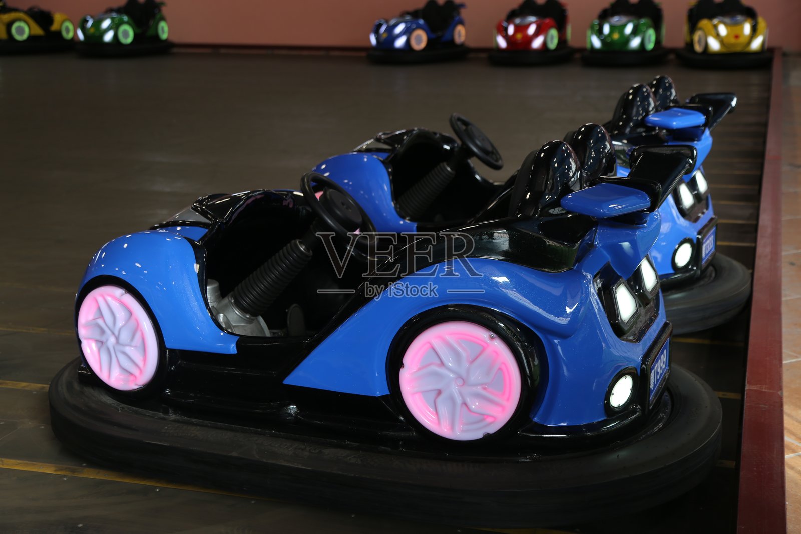 一辆蓝色的儿童车，配有粉色轮子和前灯，位于儿童游乐园的室内卡丁车赛道上供孩子们玩耍。照片摄影图片