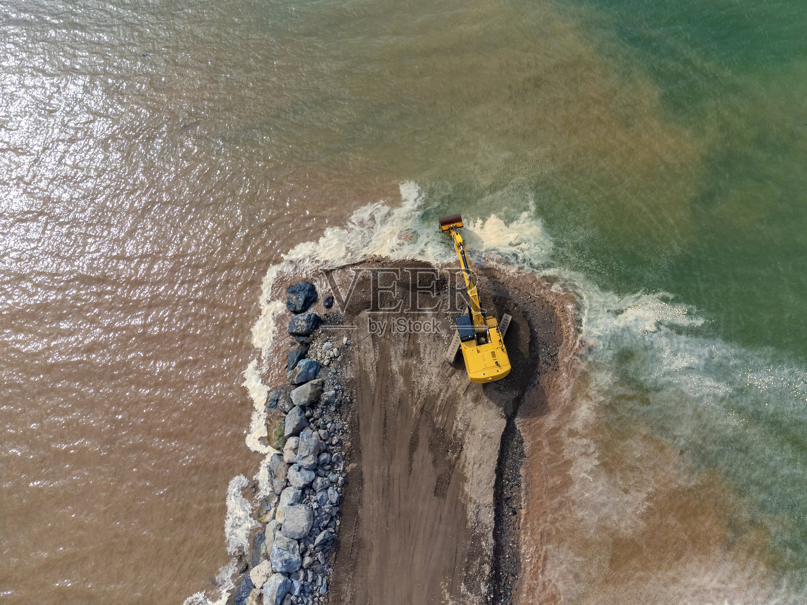 海岸、河流或水坝上工作的黄色挖掘机的无人机视角。照片摄影图片