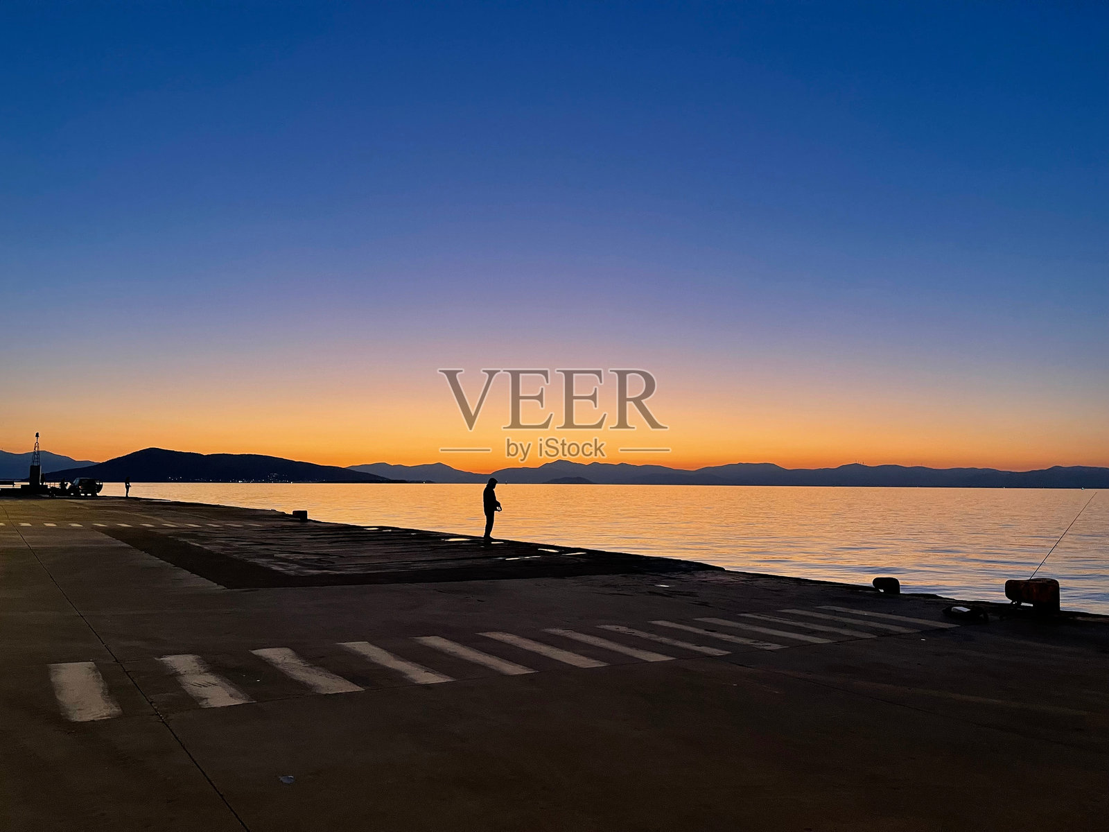 橙色日落时，清澈深蓝色天空下，港口钓鱼的男人剪影照片摄影图片