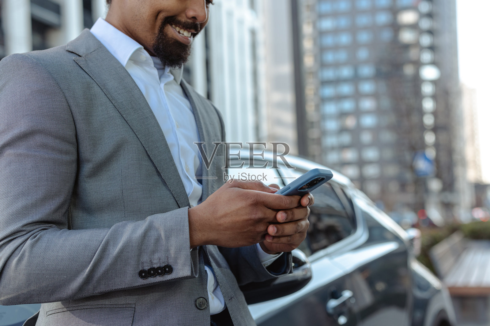 微笑的专业男士在现代城市景观中使用智能手机照片摄影图片