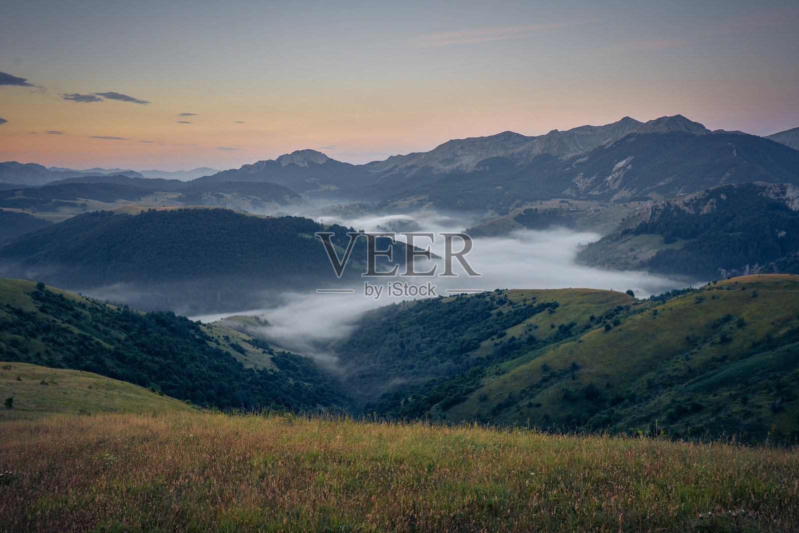 山景，薄雾笼罩山谷，天空被清晨柔和的光线染上淡淡的色彩照片摄影图片