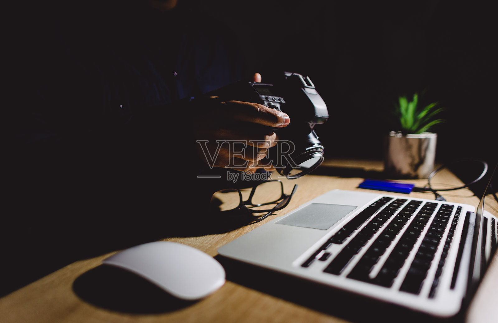 专业摄影师在笔记本电脑上工作，正在传输数码图像，摄像机悬挂在上方，周围是低光环境中的编辑设备。照片摄影图片