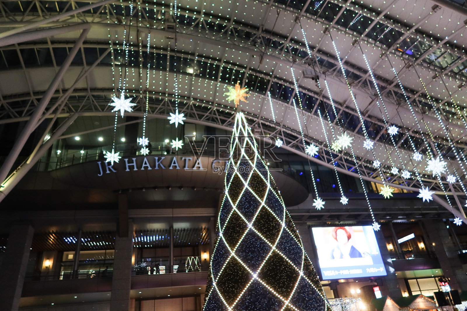 日本福冈博多JR站，圣诞市场中装饰着大圣诞树的灯光，夜晚有众多游客和户外表演。照片摄影图片