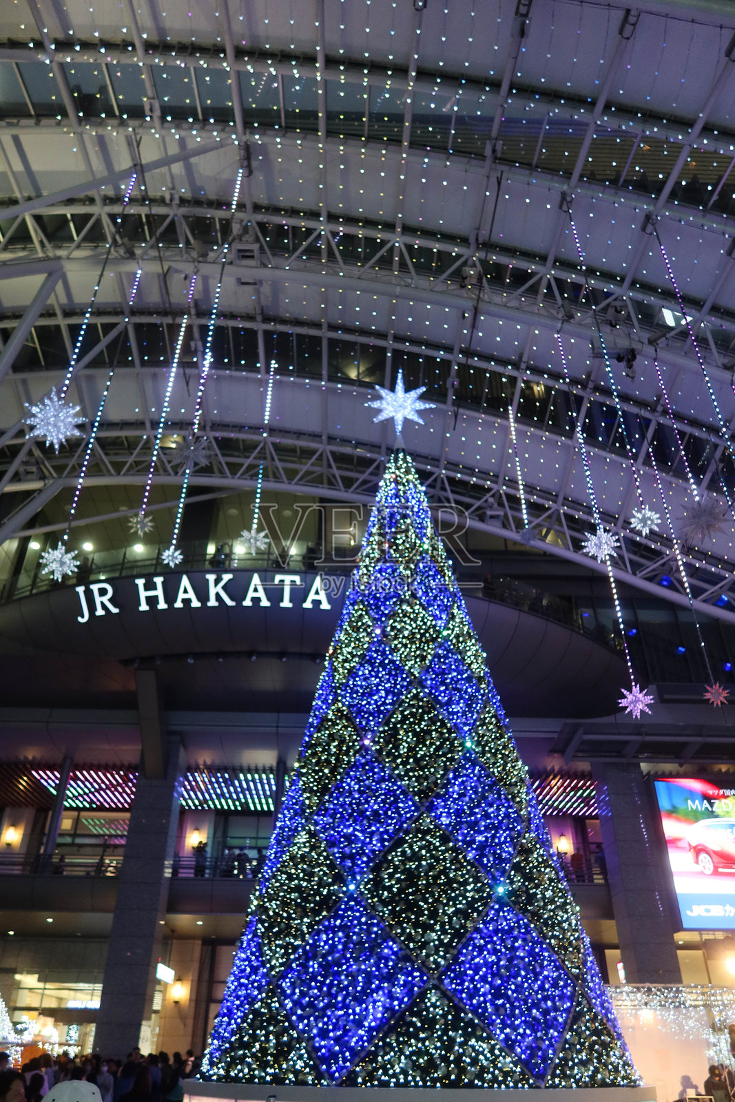 日本福冈博多JR站，圣诞市场中装饰着大圣诞树的灯光，夜晚有众多游客和户外表演。照片摄影图片