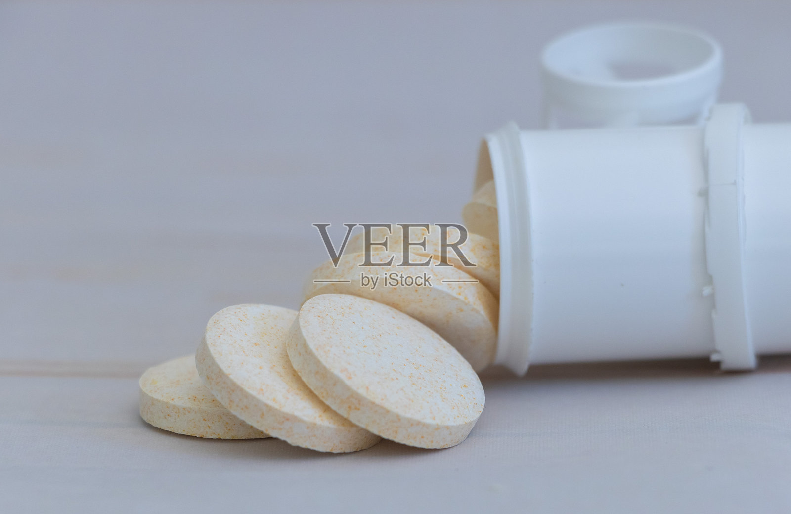 圆形米色和白色药片从打开的药瓶中洒落，背景为浅色。照片摄影图片