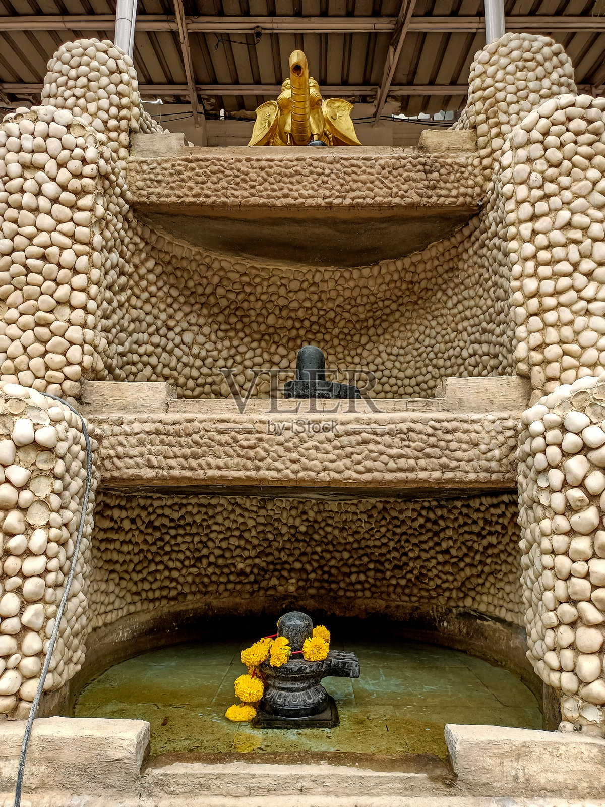 一个分层的石结构内供奉着两个湿婆神像。下层的神像装饰着黄色花朵，而较小的神像位于上层。顶部摆放着一尊金色的牛神南迪雕像。照片摄影图片