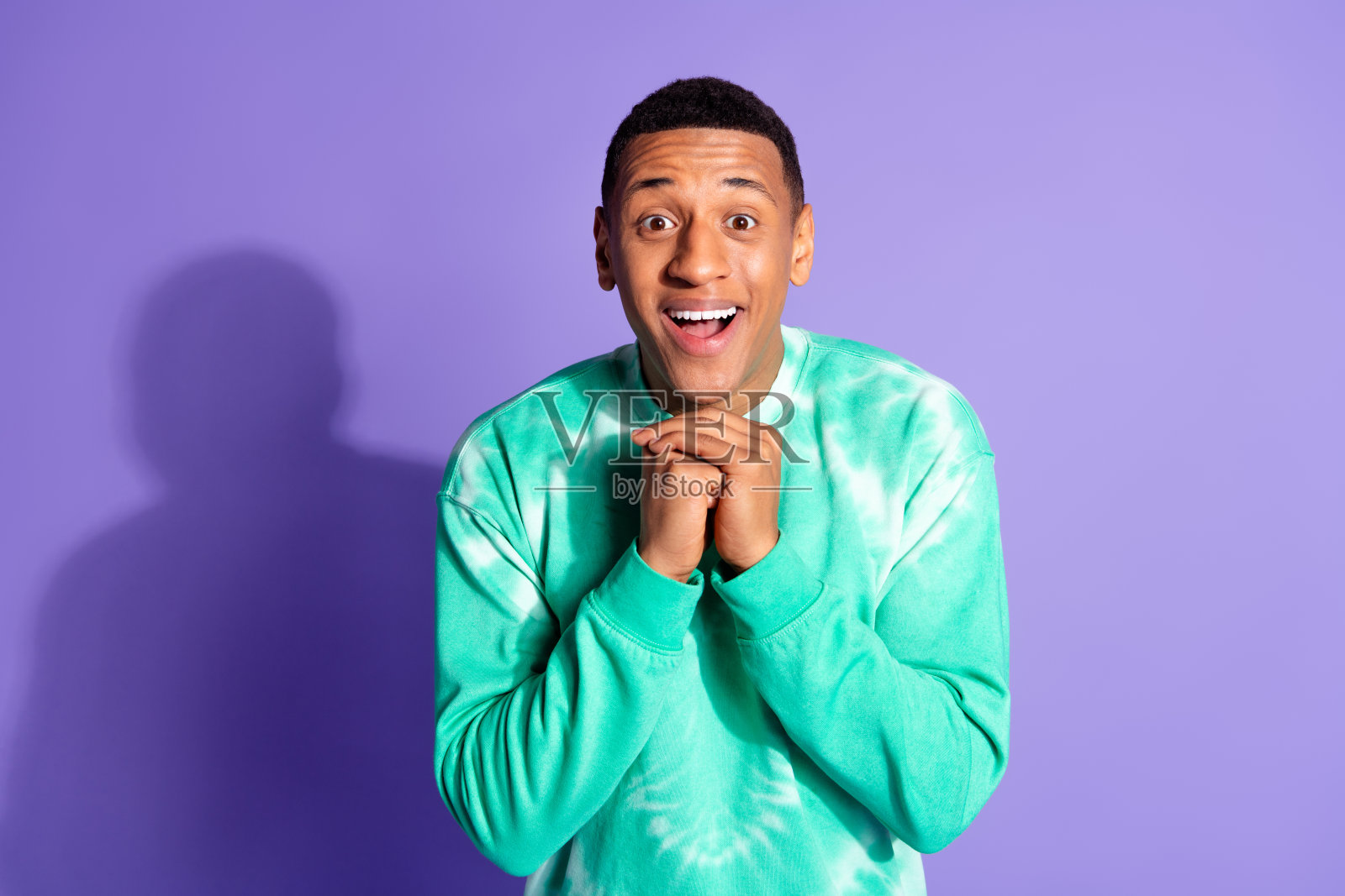 兴奋的搞笑男士穿着青色卫衣，微笑着，背景为紫色的空旷空间。照片摄影图片