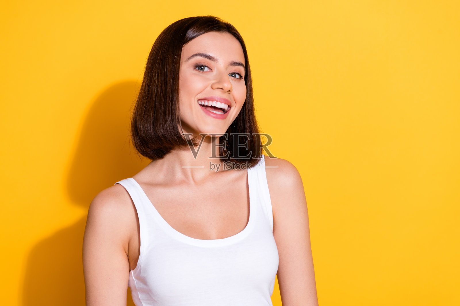 穿着时尚白色服装的迷人年轻女孩，面带灿烂的笑容，背景为黄色。照片摄影图片