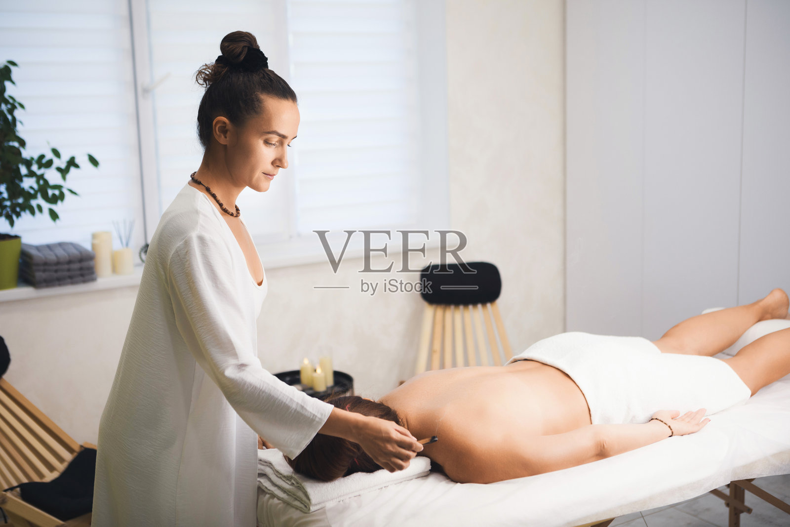 按摩治疗师在沙龙中为面朝下躺着的客户使用巴洛圣木棒，特写，选择性对焦。照片摄影图片