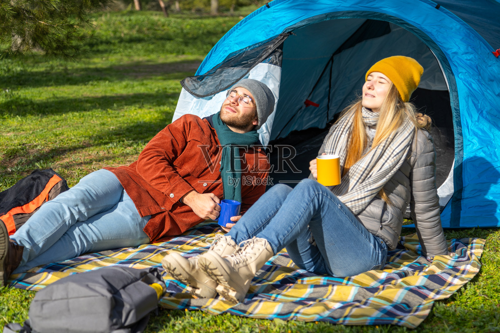快乐的露营者在帐篷外放松，享受热饮和阳光照片摄影图片