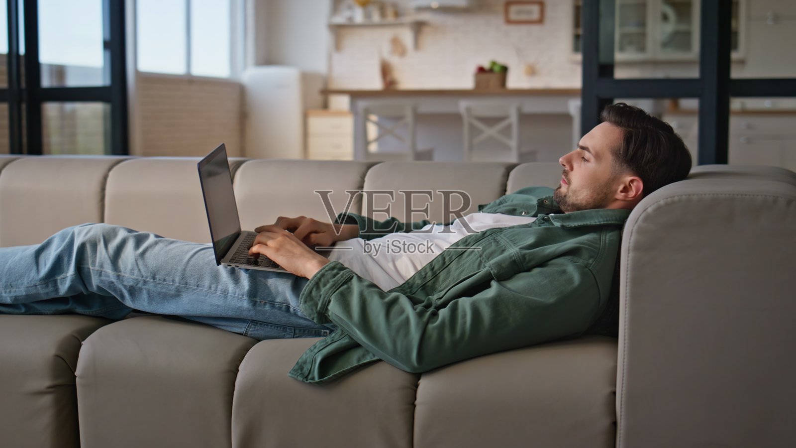 男人在家里的沙发上舒适地躺着使用笔记本电脑。忙碌的自由职业者工作。照片摄影图片