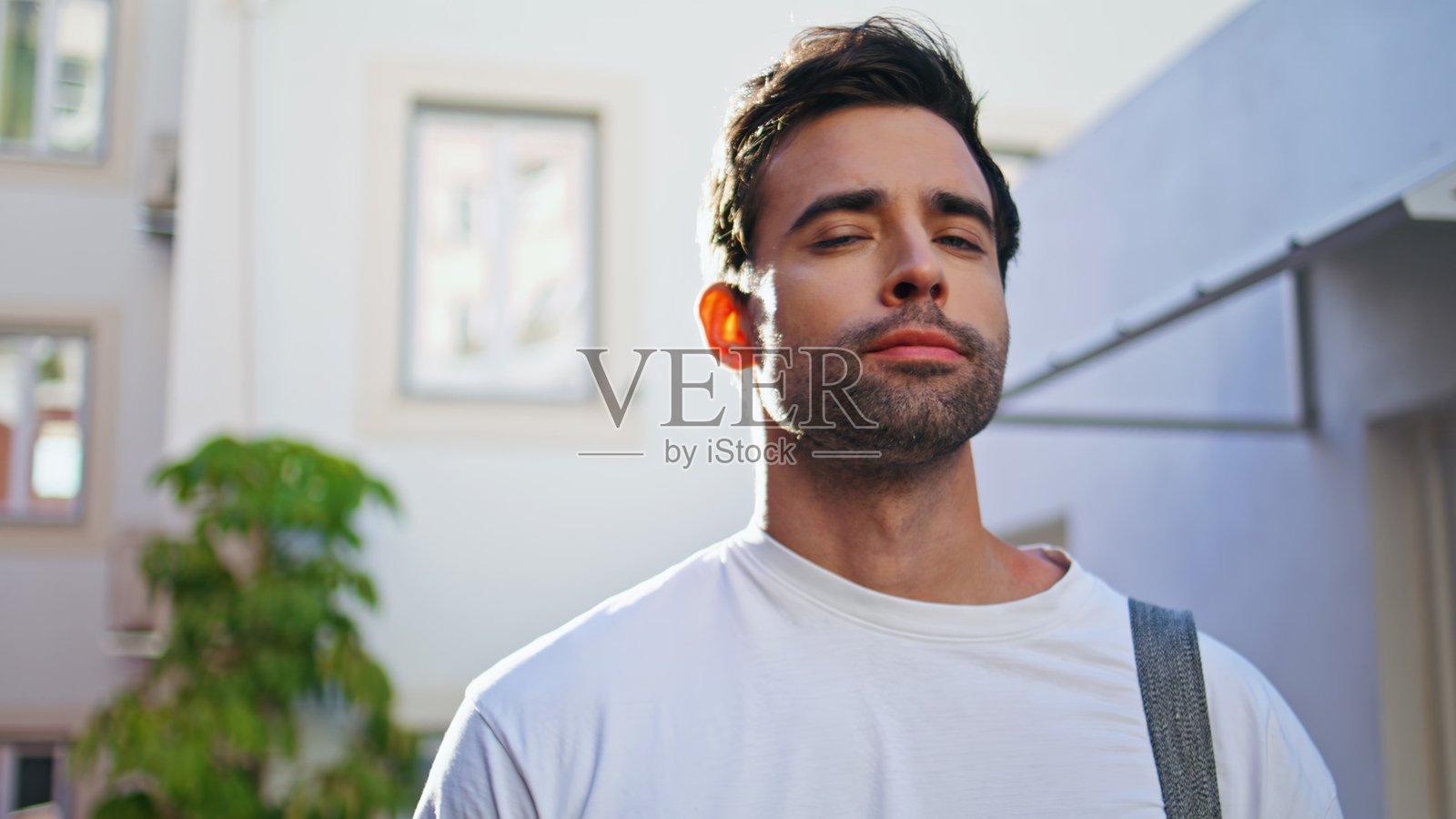 自信的男子在阳光明媚的街道上穿着T恤的特写。西班牙裔男性的肖像。照片摄影图片