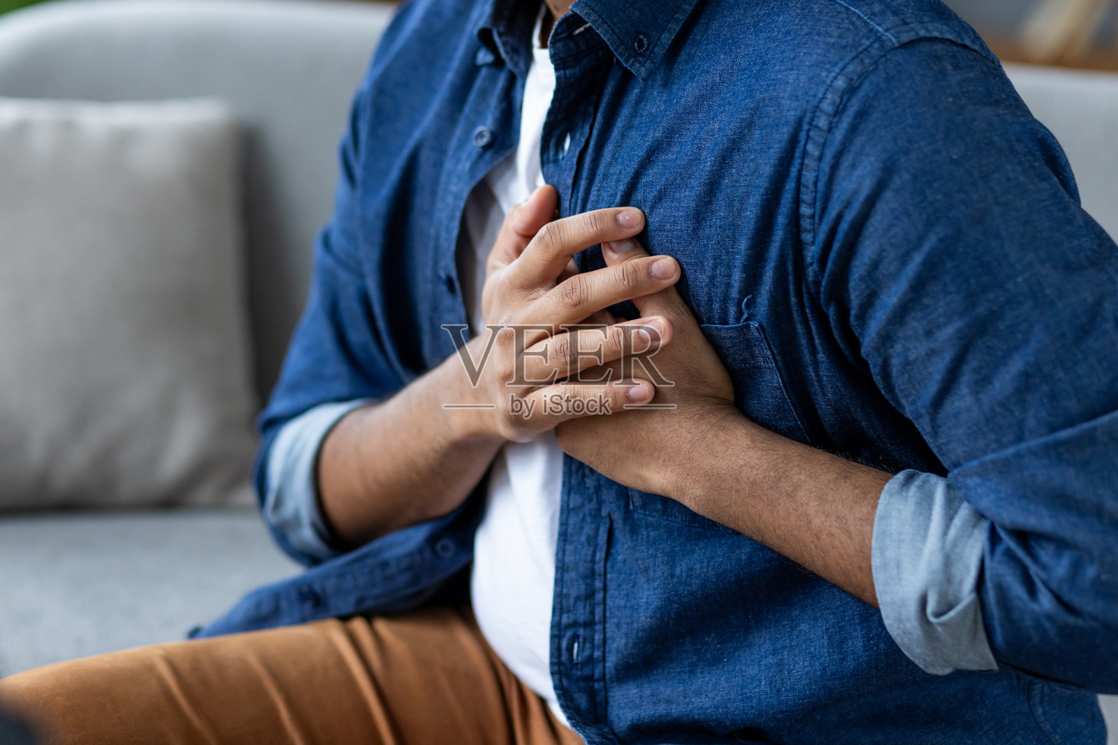 男子双手放在心口，感到剧烈疼痛，心脏病发作，坐在家中的客厅沙发上特写镜头照片摄影图片