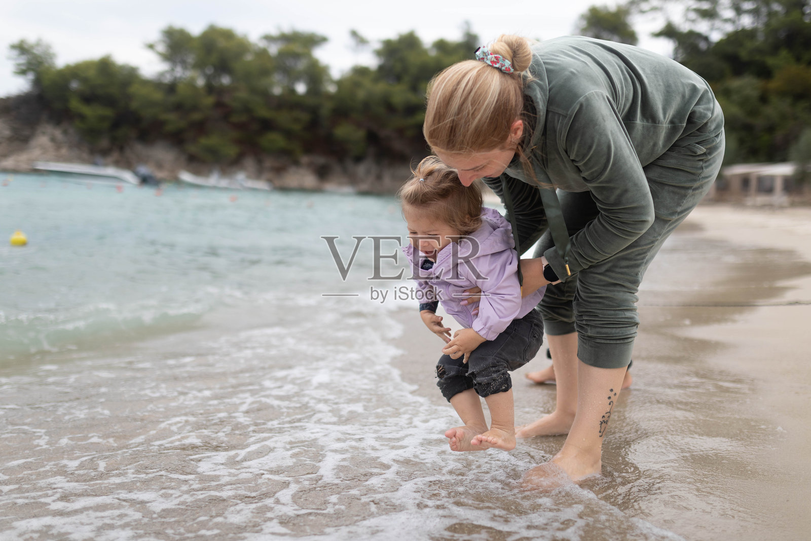 一位母亲帮助女儿用脚触碰海水。照片摄影图片