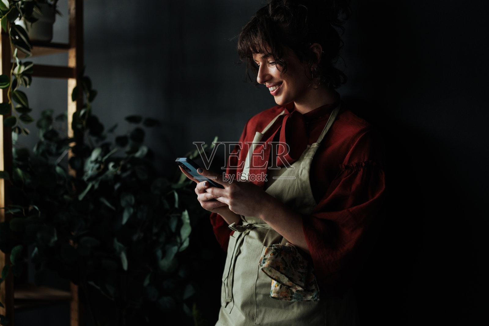 花店里微笑的花艺师正在使用智能手机照片摄影图片