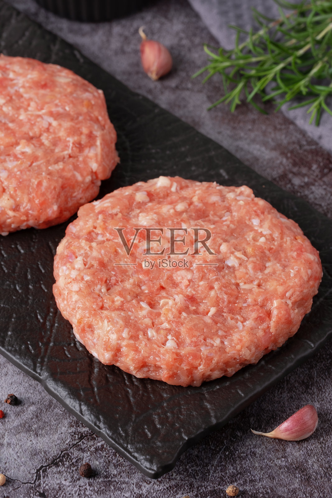 新鲜的肉饼准备好烹饪，配有香草和大蒜，放在深色盘子上照片摄影图片