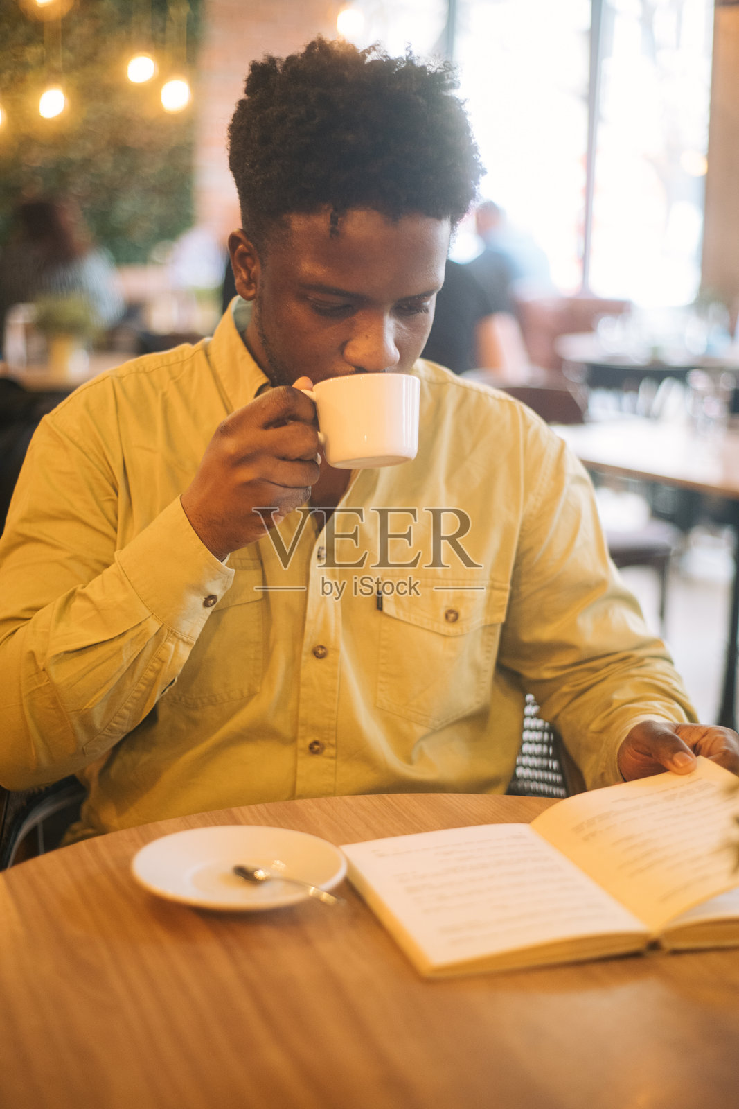 一位帅气的黑人男子在咖啡馆里阅读一本书并喝咖啡照片摄影图片