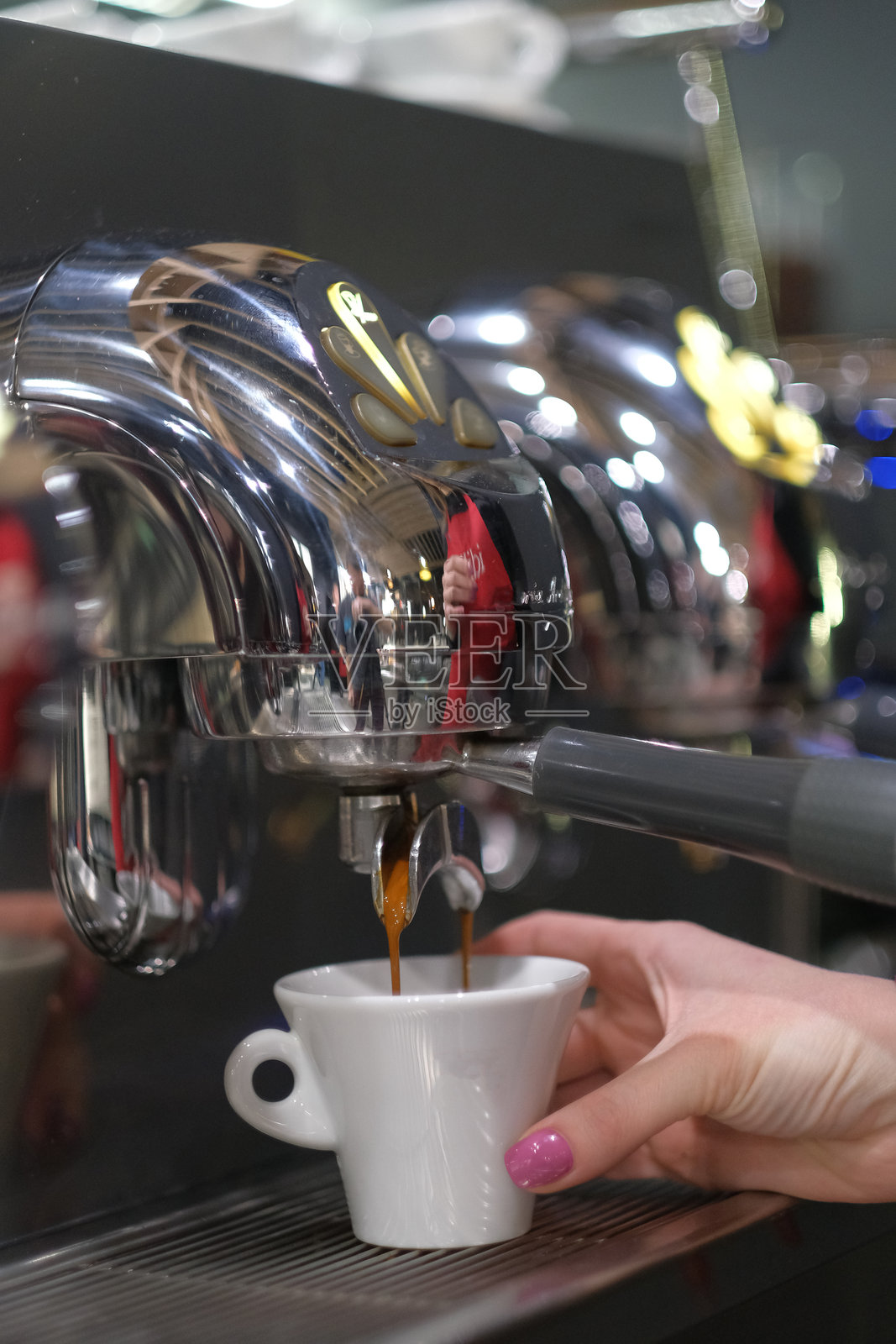 女性的手在一台铬合金商业咖啡机下托着一个白色杯子，浓缩咖啡正在被拉入杯中，新鲜冲泡的浓缩咖啡。照片摄影图片