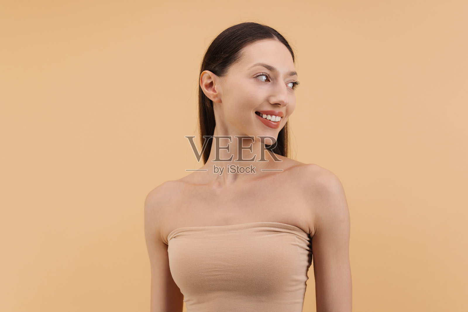 微笑的女性，皮肤完美，侧目而视，背景为米色。美容概念。照片摄影图片