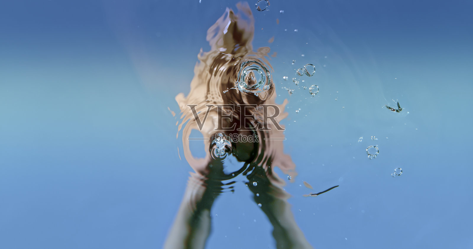 手伸入水中，形成圆形涟漪图案，蓝色背景照片摄影图片