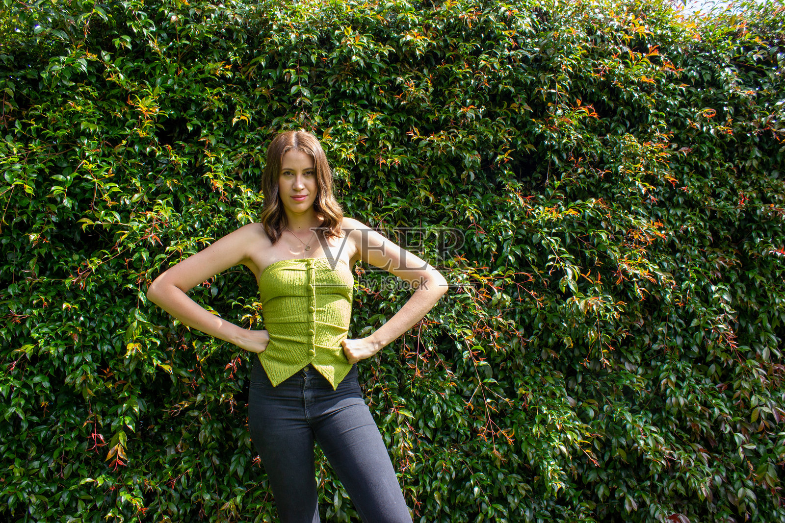 美丽的女性在一面叶子墙前摆姿势。照片摄影图片