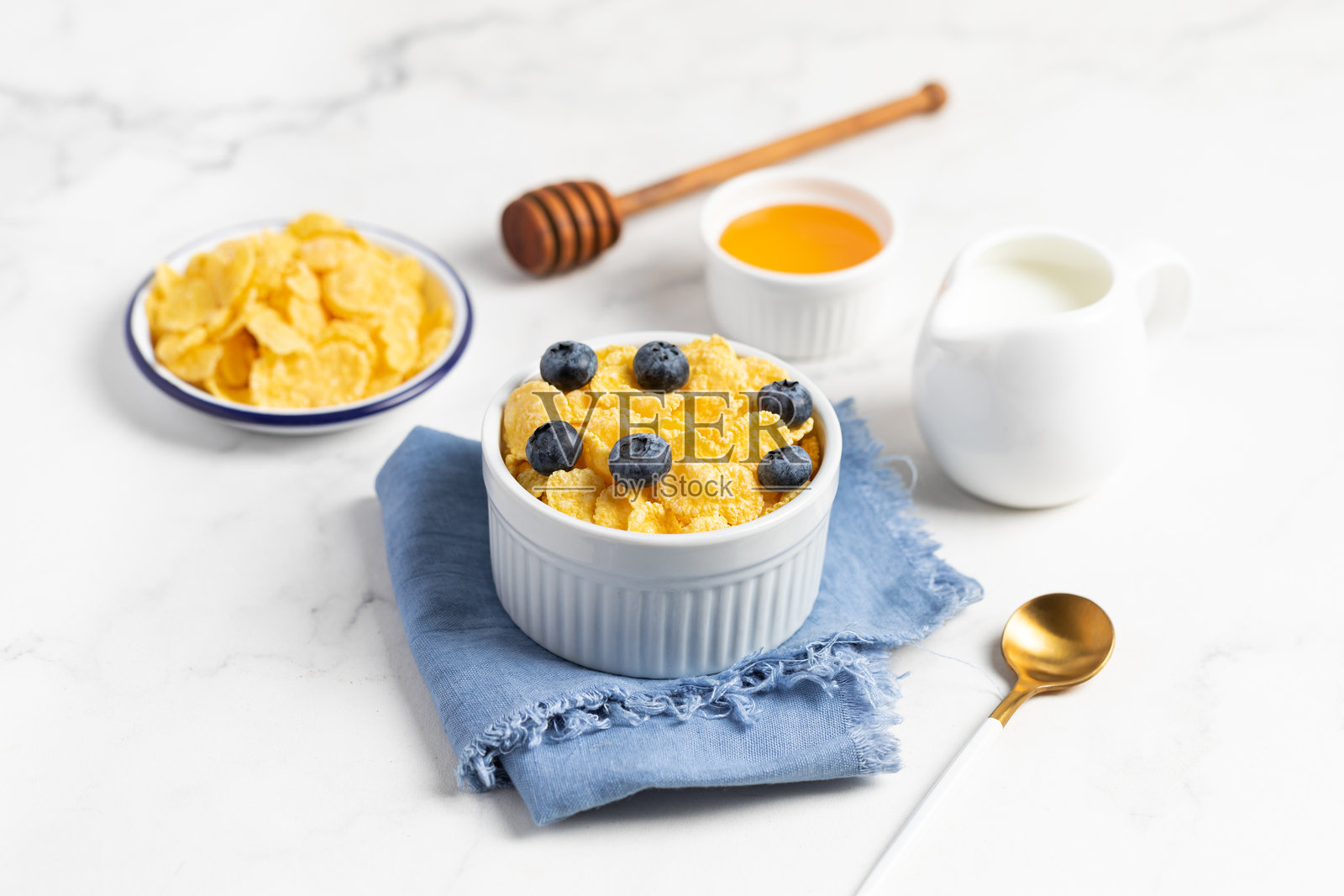 碗里装着玉米片和蓝莓，旁边有牛奶，背景明亮，早餐。照片摄影图片