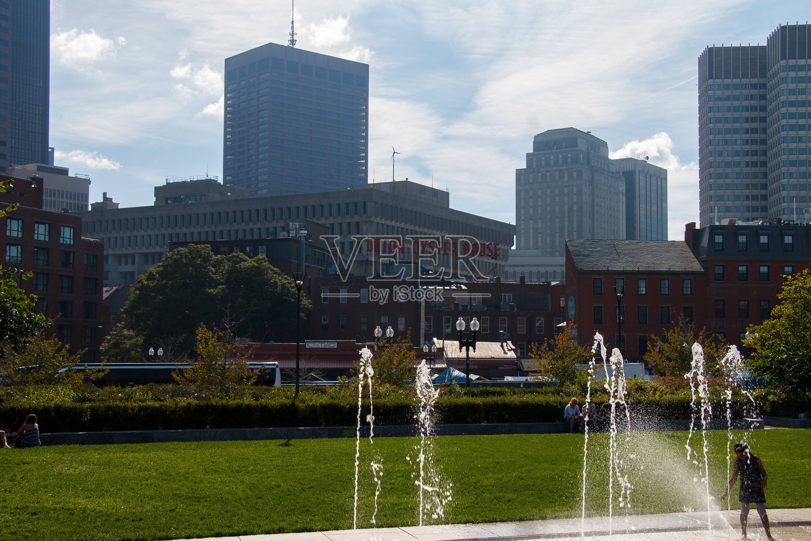 人们在美国马萨诸塞州波士顿市中心的罗斯·肯尼迪绿道上享受阳光明媚的一天，背景是海关大楼和办公摩天大楼。照片摄影图片