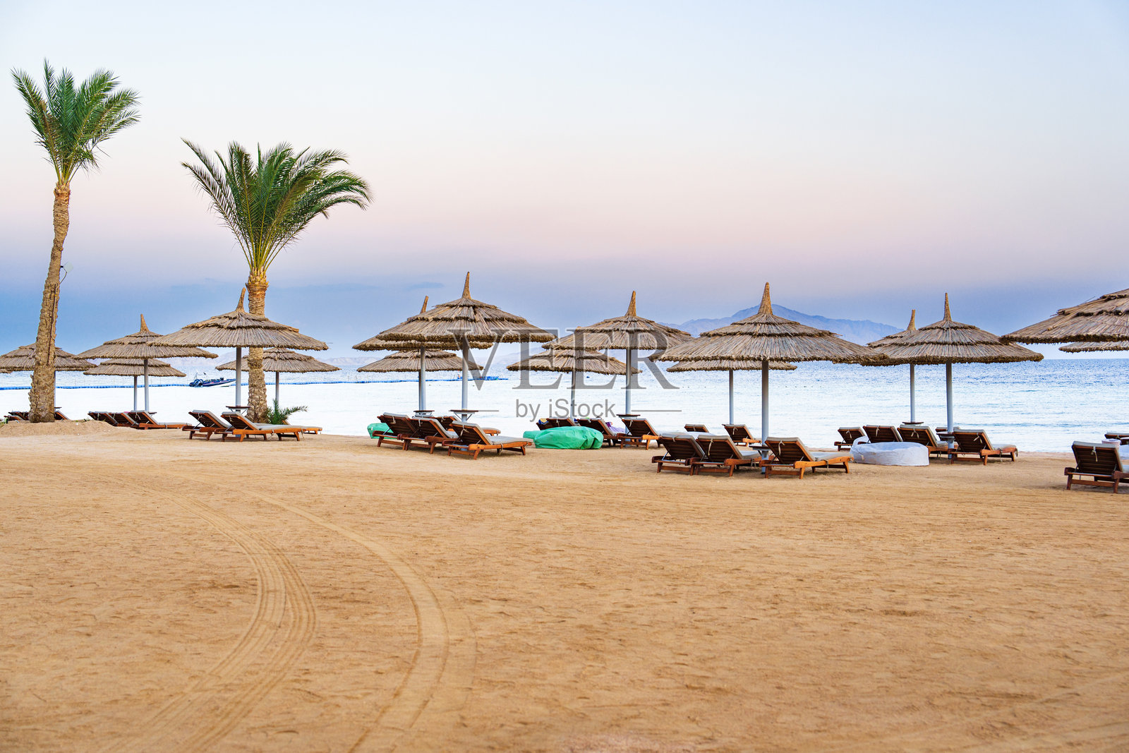 日落时分的放松海滩景色，海岸线上有草编伞和躺椅。照片摄影图片