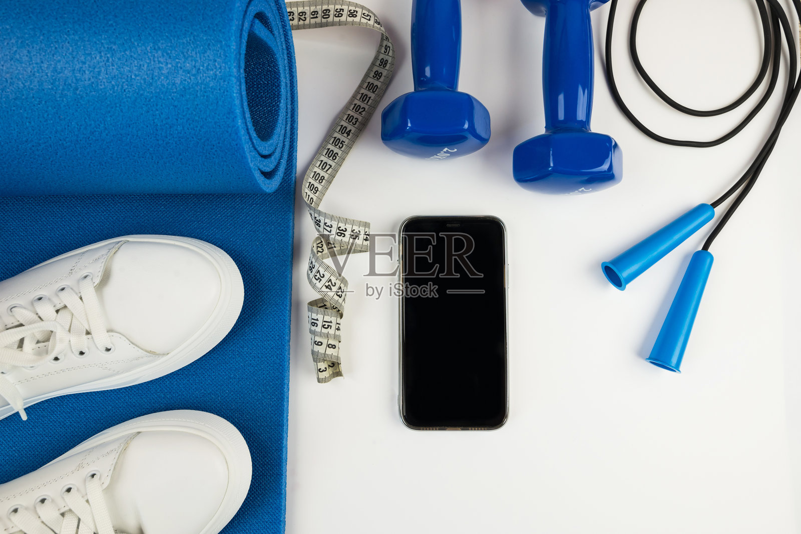 运动配件的概念。白色运动鞋、蓝色哑铃、蓝色瑜伽垫及其他运动器材的照片。照片摄影图片