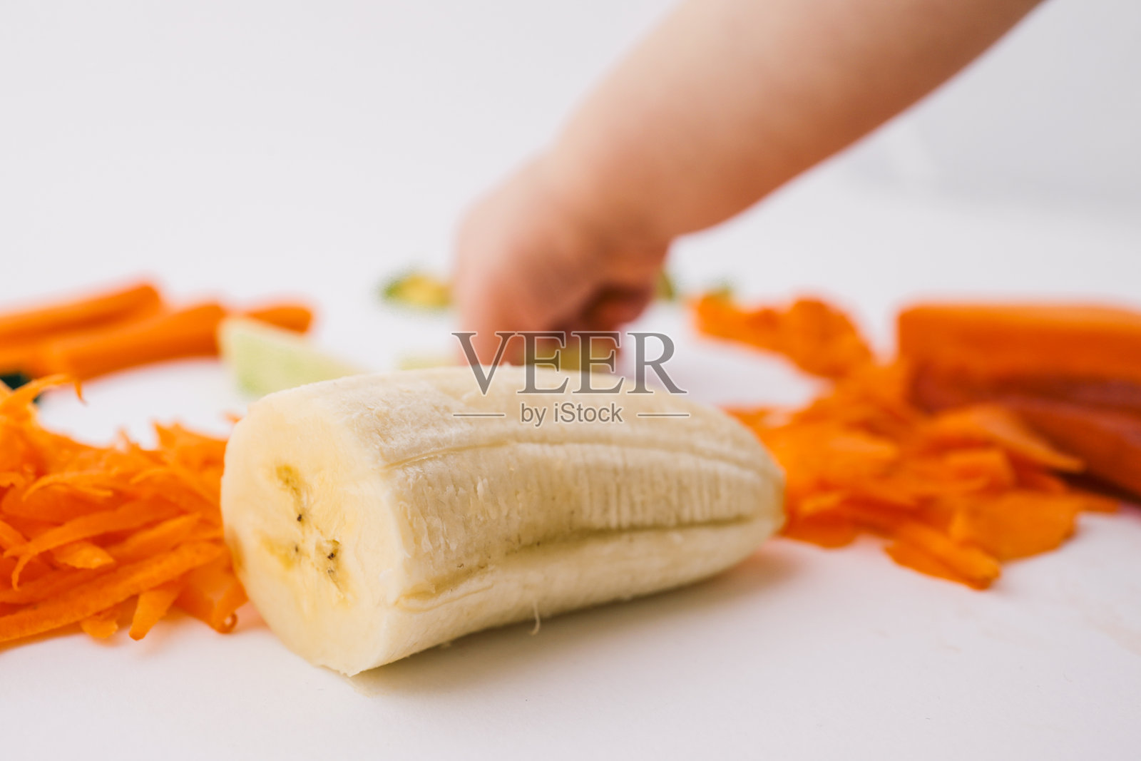 一个孩子的手伸向白色表面上新鲜切好的蔬菜。包括切丁的鳄梨、胡萝卜、苹果片、甜椒和番茄块。极简主义的食物构图。照片摄影图片