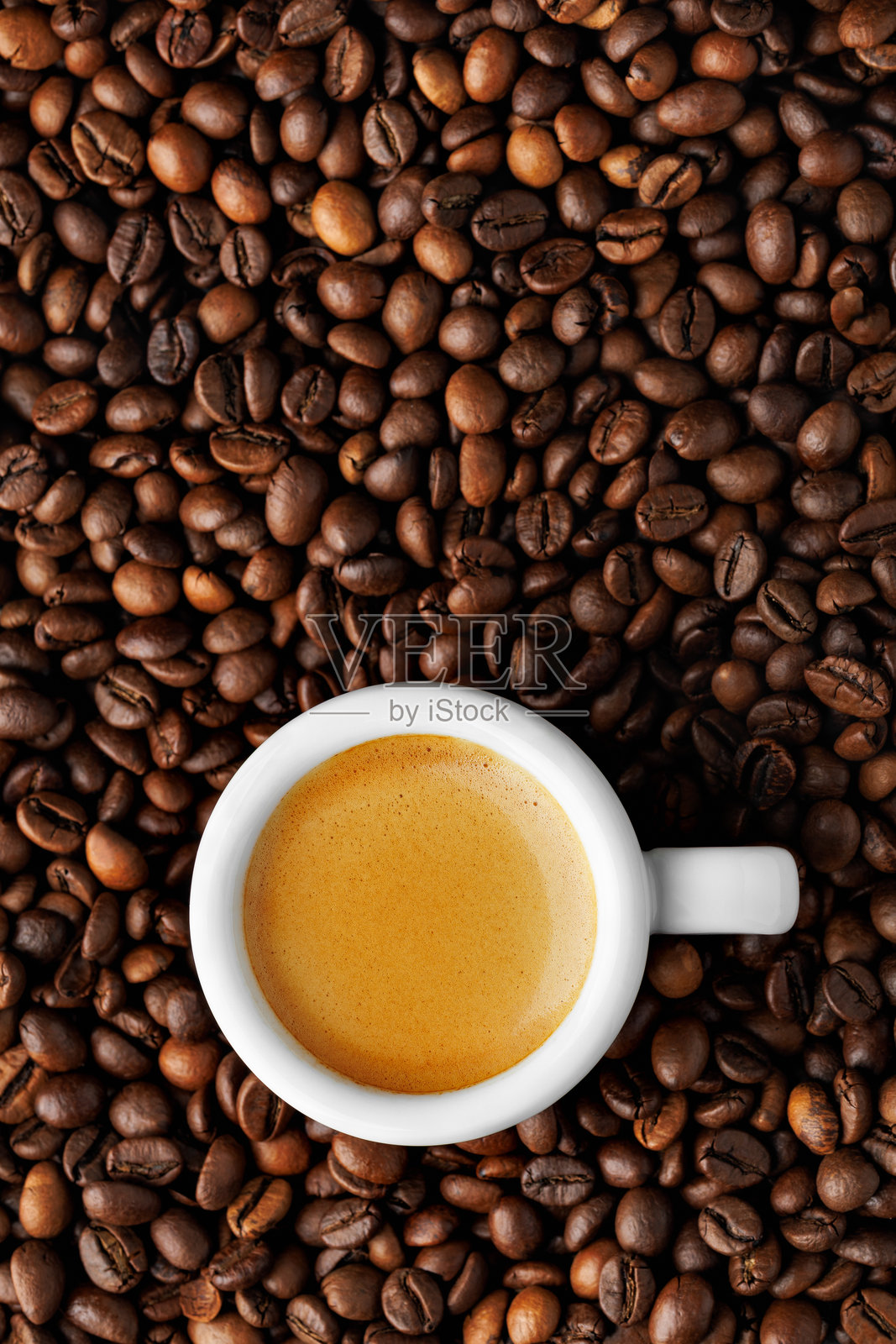 白色浓缩咖啡杯俯视图，置于烘焙咖啡豆上，突显丰富的奶泡，为咖啡爱好者营造背景。垂直拍摄。照片摄影图片