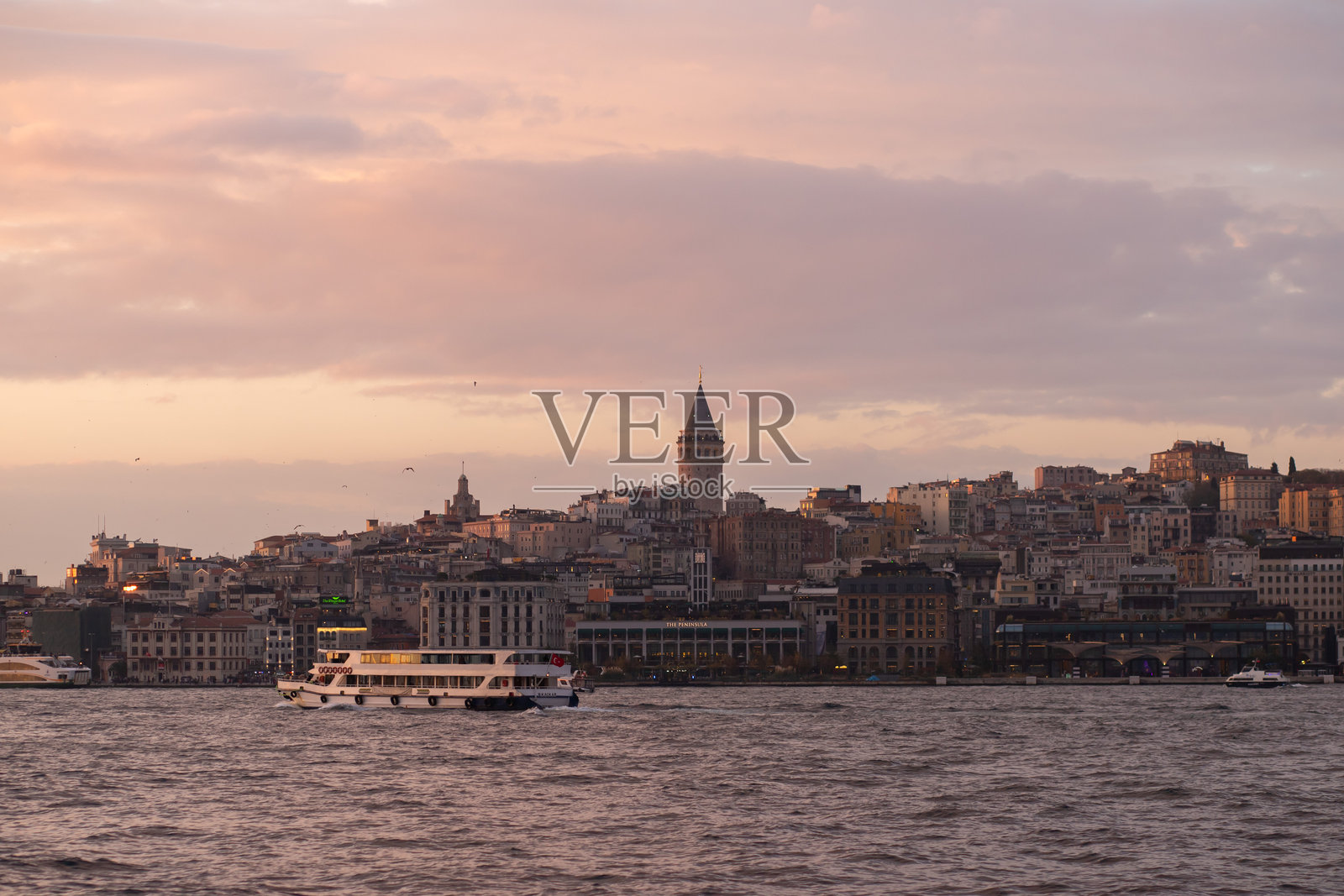 一个沐浴在金色时光中的海滨城市，水面上有一艘渡轮，背景是一座历史悠久的塔楼，土耳其伊斯坦布尔，2024年11月20日照片摄影图片