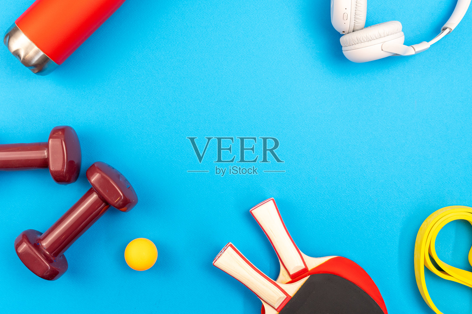 健身配件如哑铃、乒乓球拍和阻力带排列在充满活力的蓝色背景上，宣传健康生活方式照片摄影图片