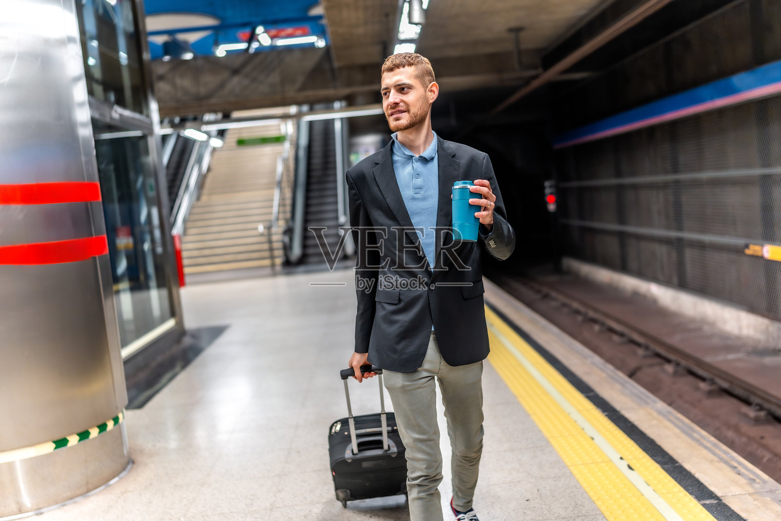商人在地铁站台上走动，手里提着行李和咖啡。照片摄影图片