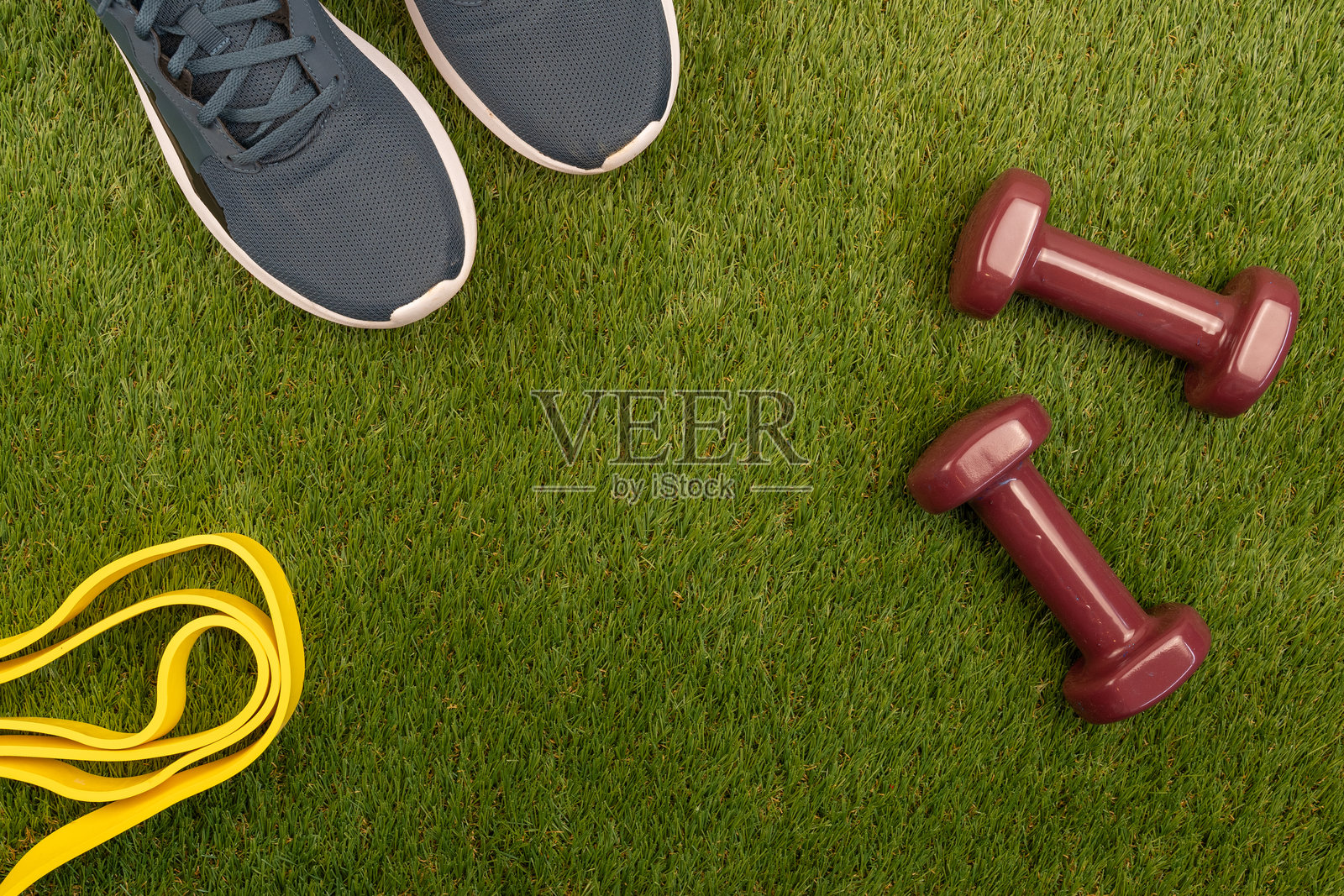 健身配件如哑铃、阻力带和跑鞋放在草地上，邀请进行户外训练照片摄影图片