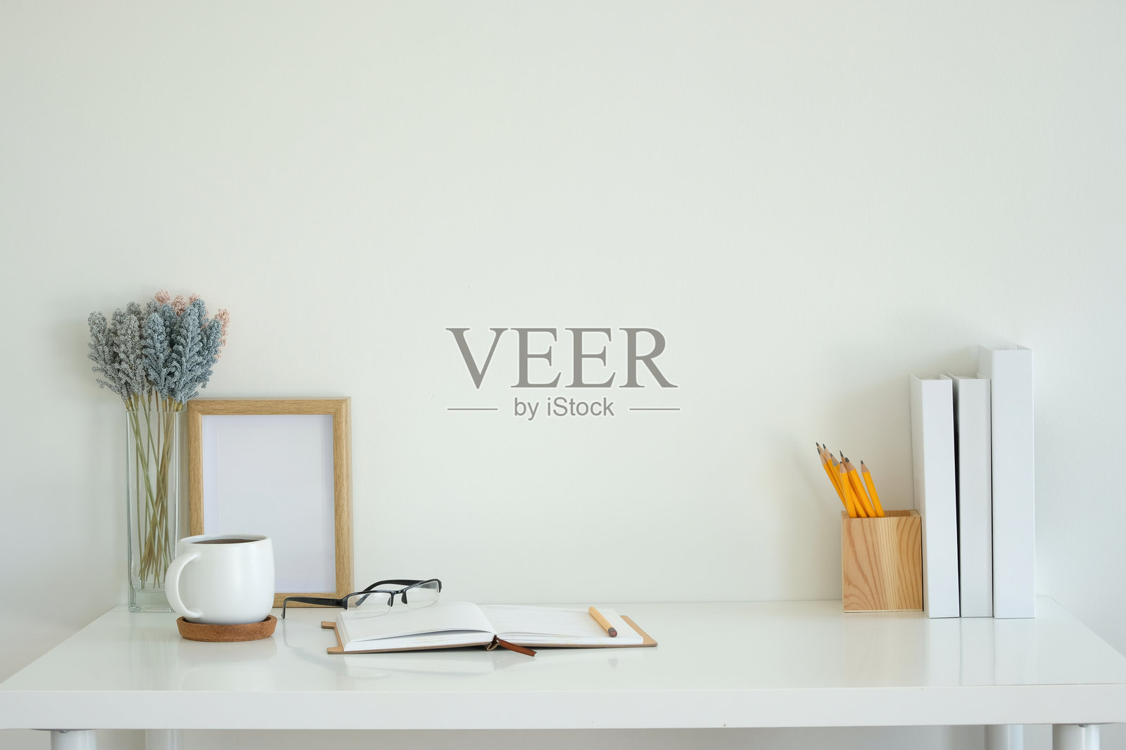 白色桌子上放着一本打开的笔记本、一只白色咖啡杯、一副眼镜和一支铅笔。照片摄影图片